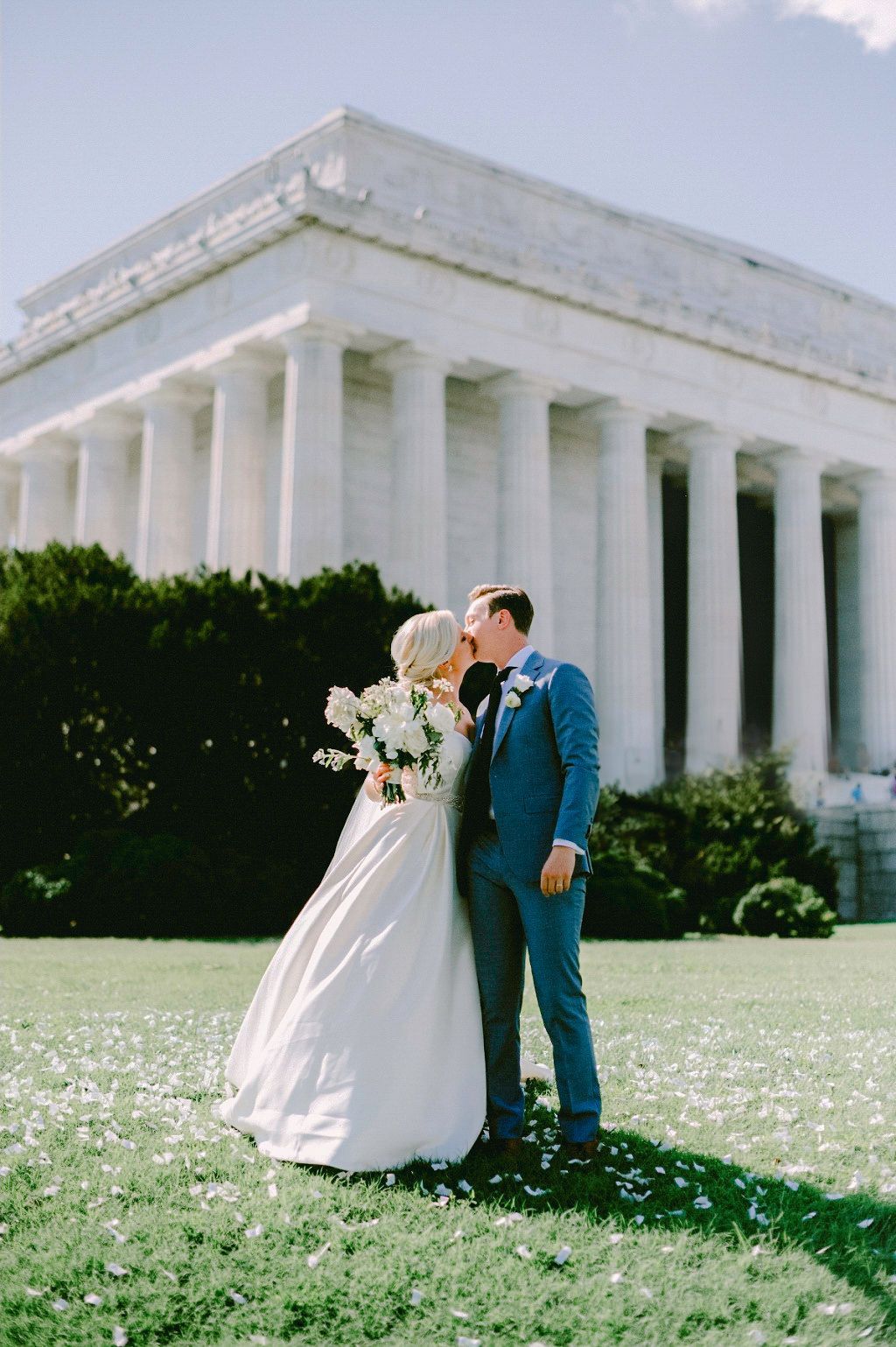 A wedding couple shares an intimate moment in front of the white columns of the Lincoln Memorial on a sunny spring day.