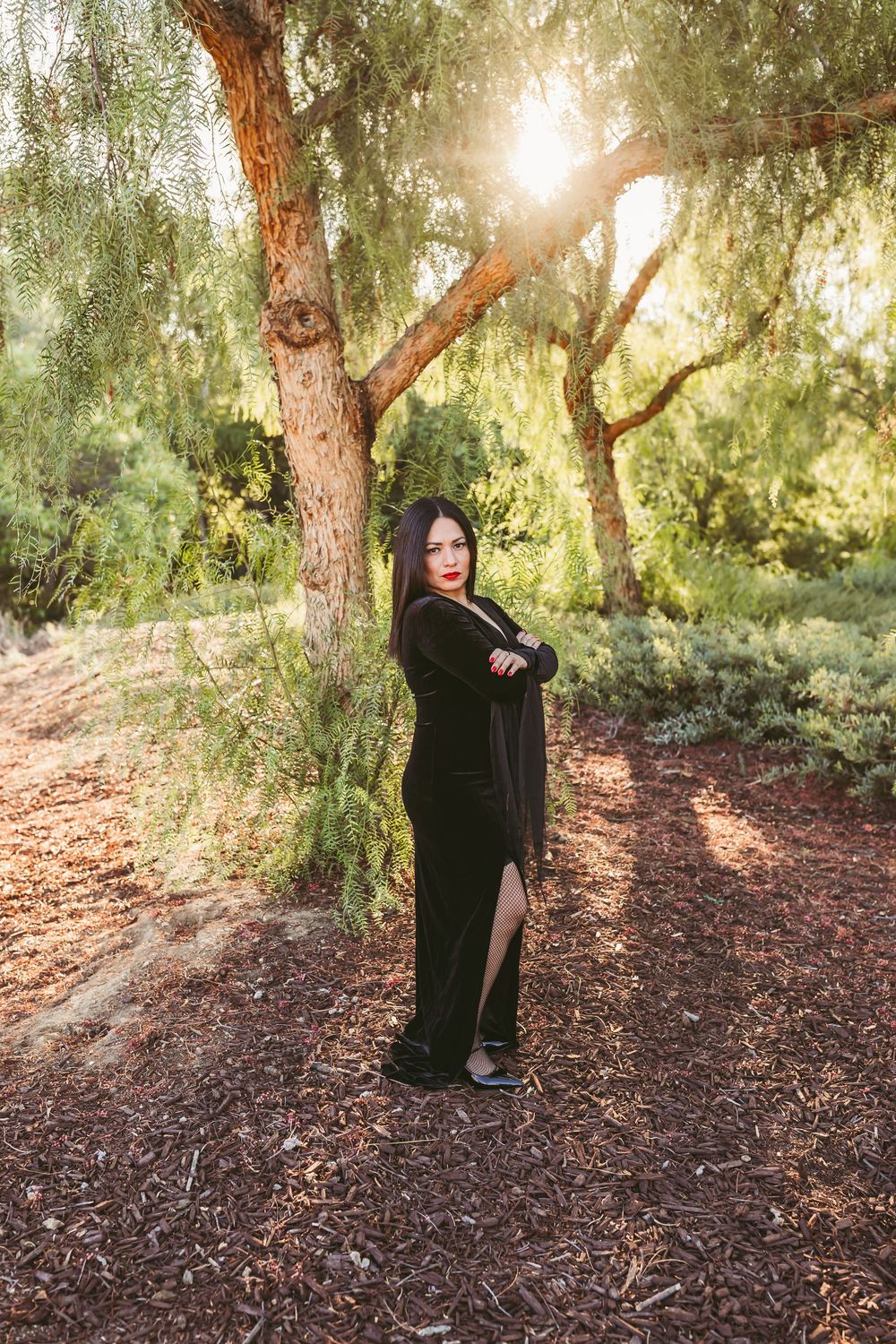 A serene photo shoot in a wooded area with willow trees and dappled sunlight filtering through the branches.