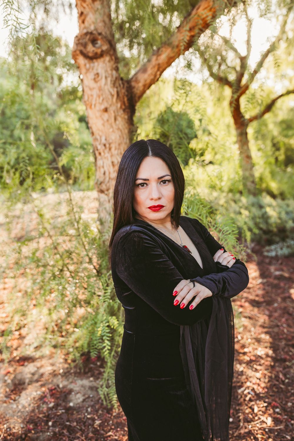 Fashion portrait series in a wooded setting showing dramatic poses in a black velvet dress against autumn foliage.