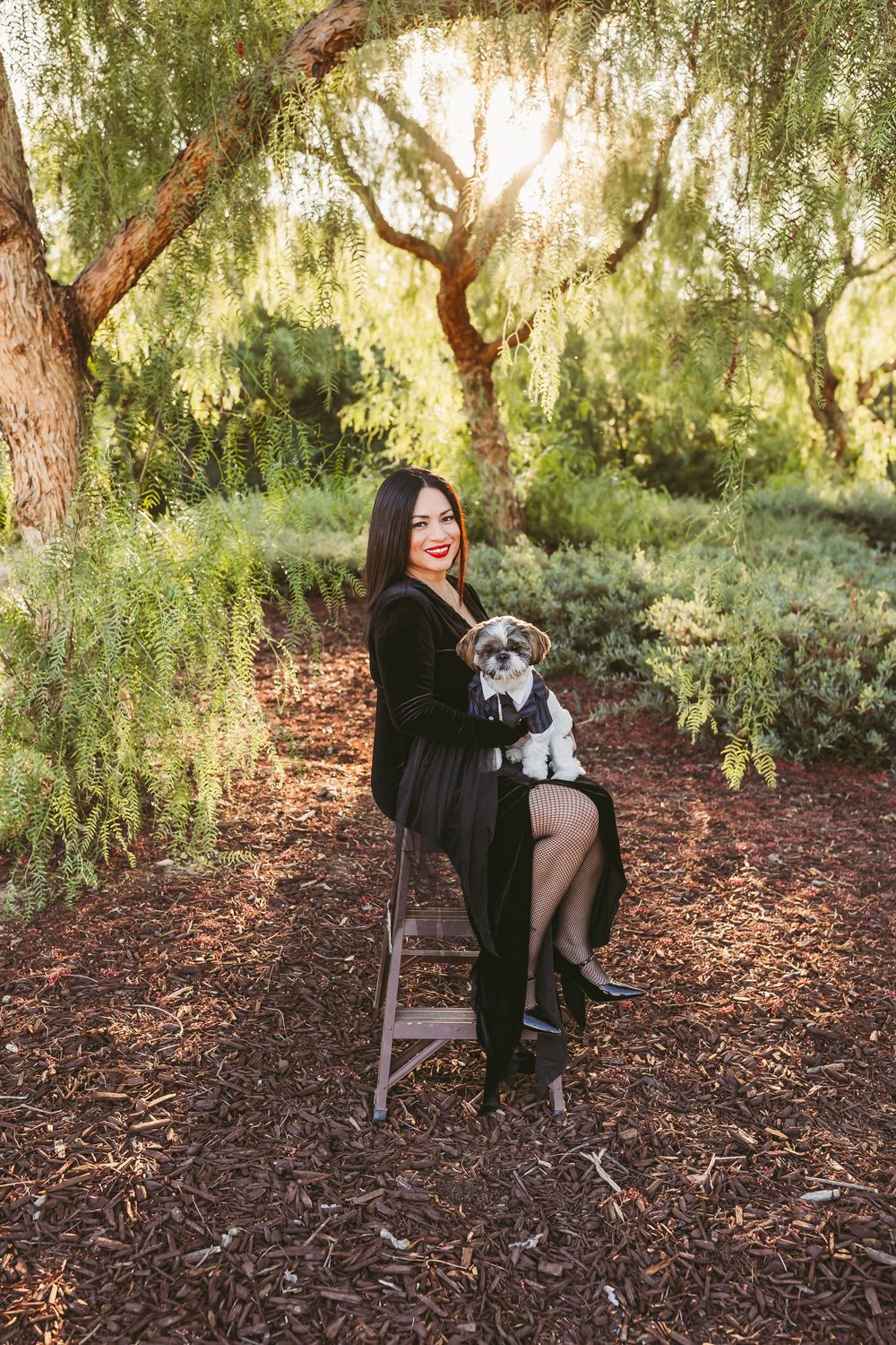 Stylish portrait session in a park setting with black velvet dress and dramatic poses on vintage chair.