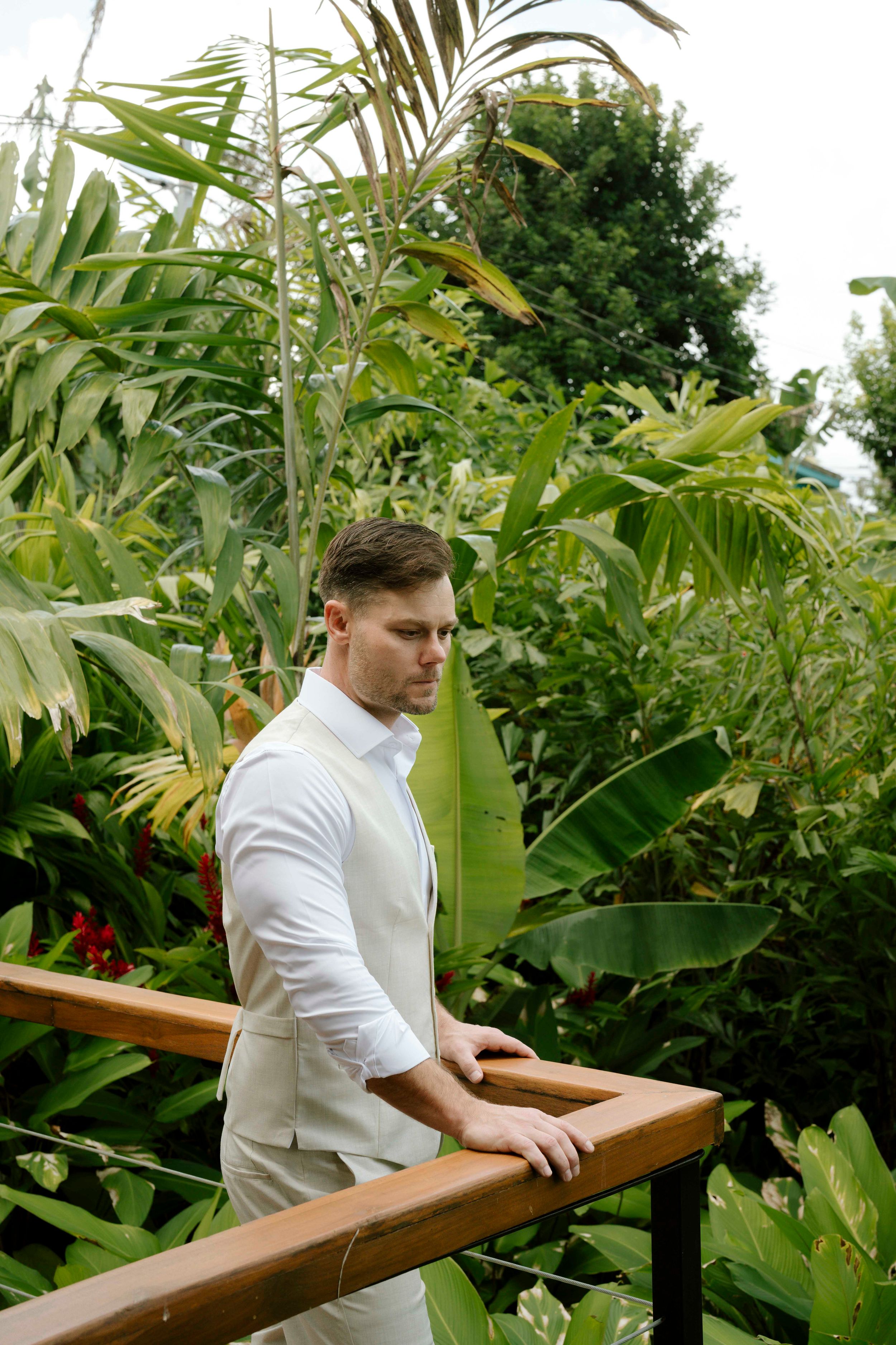 Tropical garden setting with wooden railings surrounded by large monstera and palm leaves.
