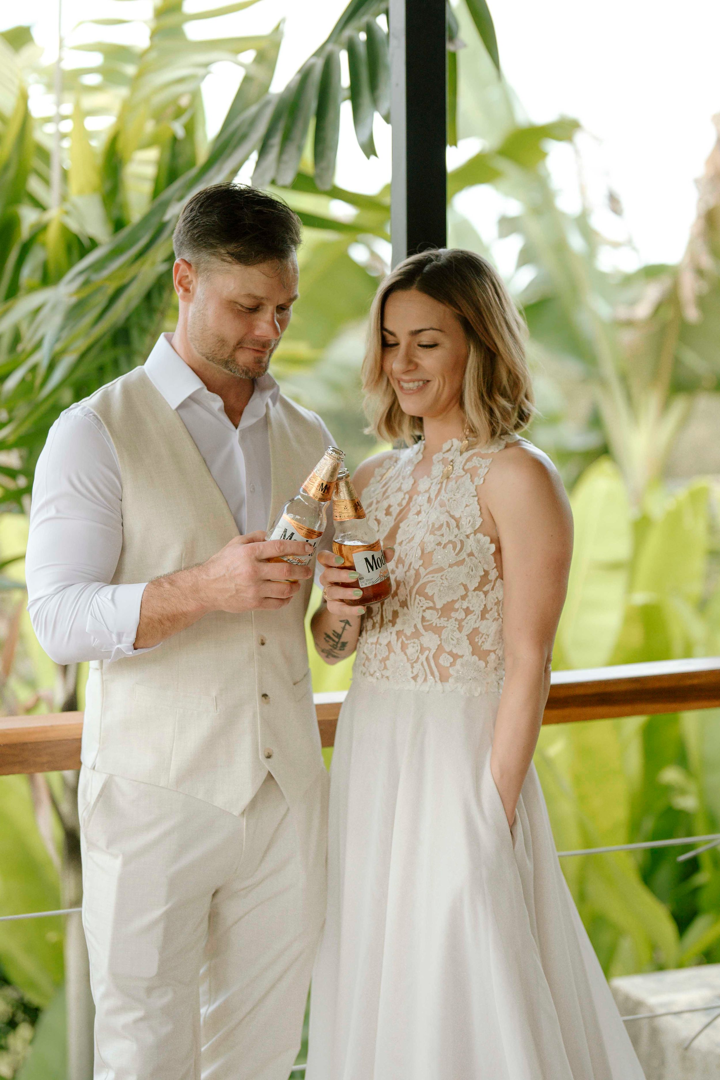Couple in white attire sharing an intimate moment while holding drinks in a tropical setting.