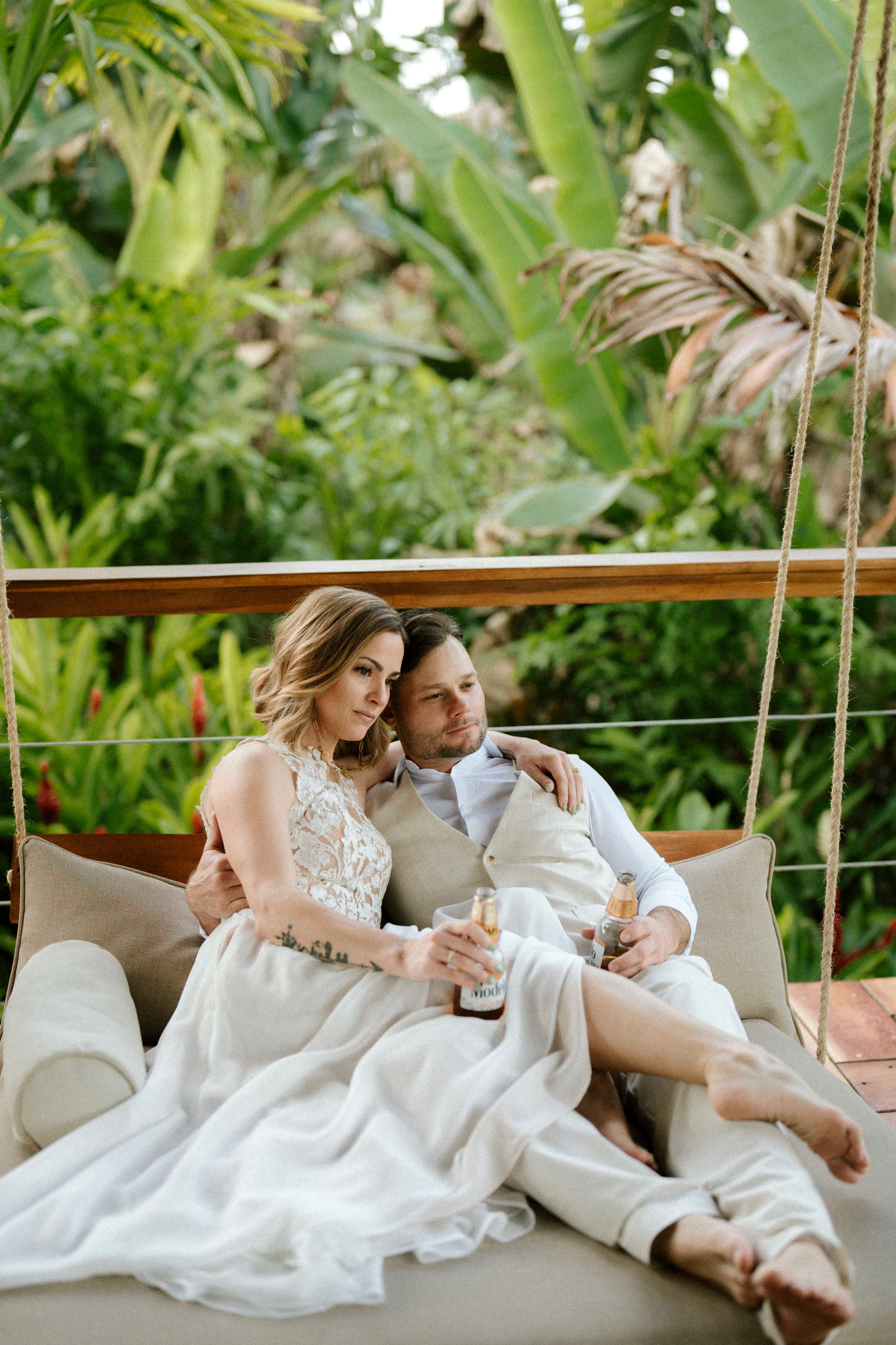 Newlyweds relaxing together on a white couch surrounded by lush tropical greenery.