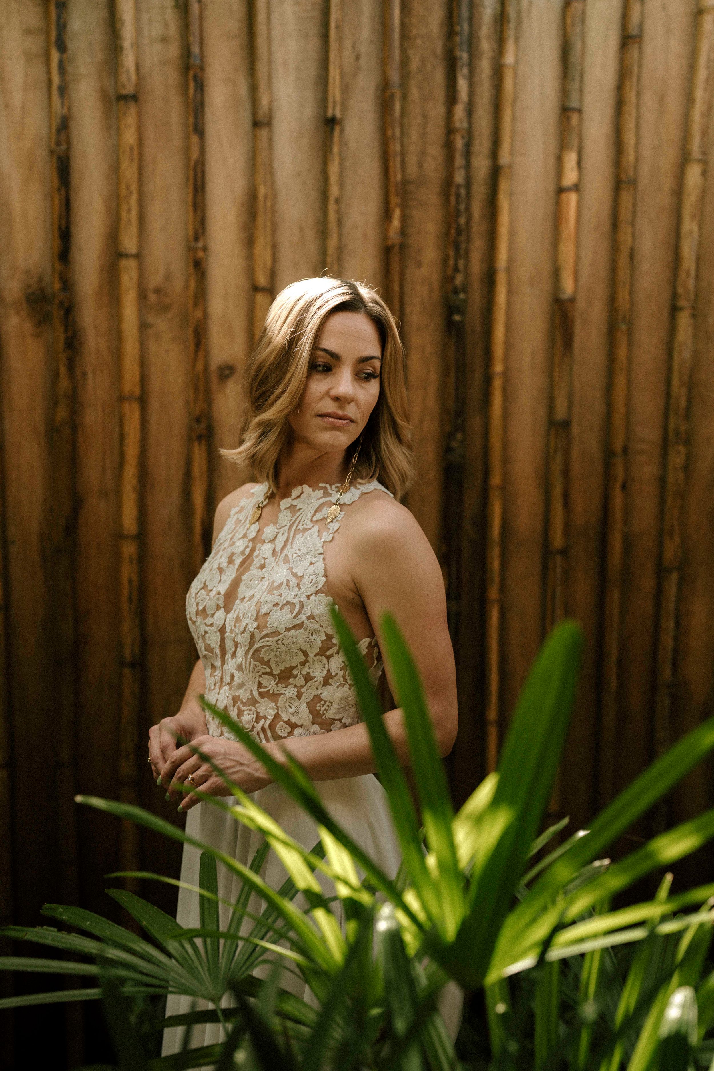 Elegant bridal portrait against a bamboo fence with tropical plants in the foreground.