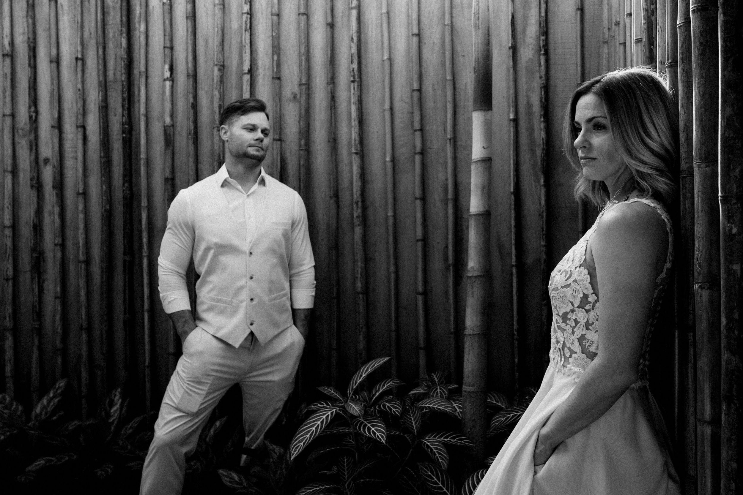 Wedding couple posing against a wooden fence backdrop in natural lighting.