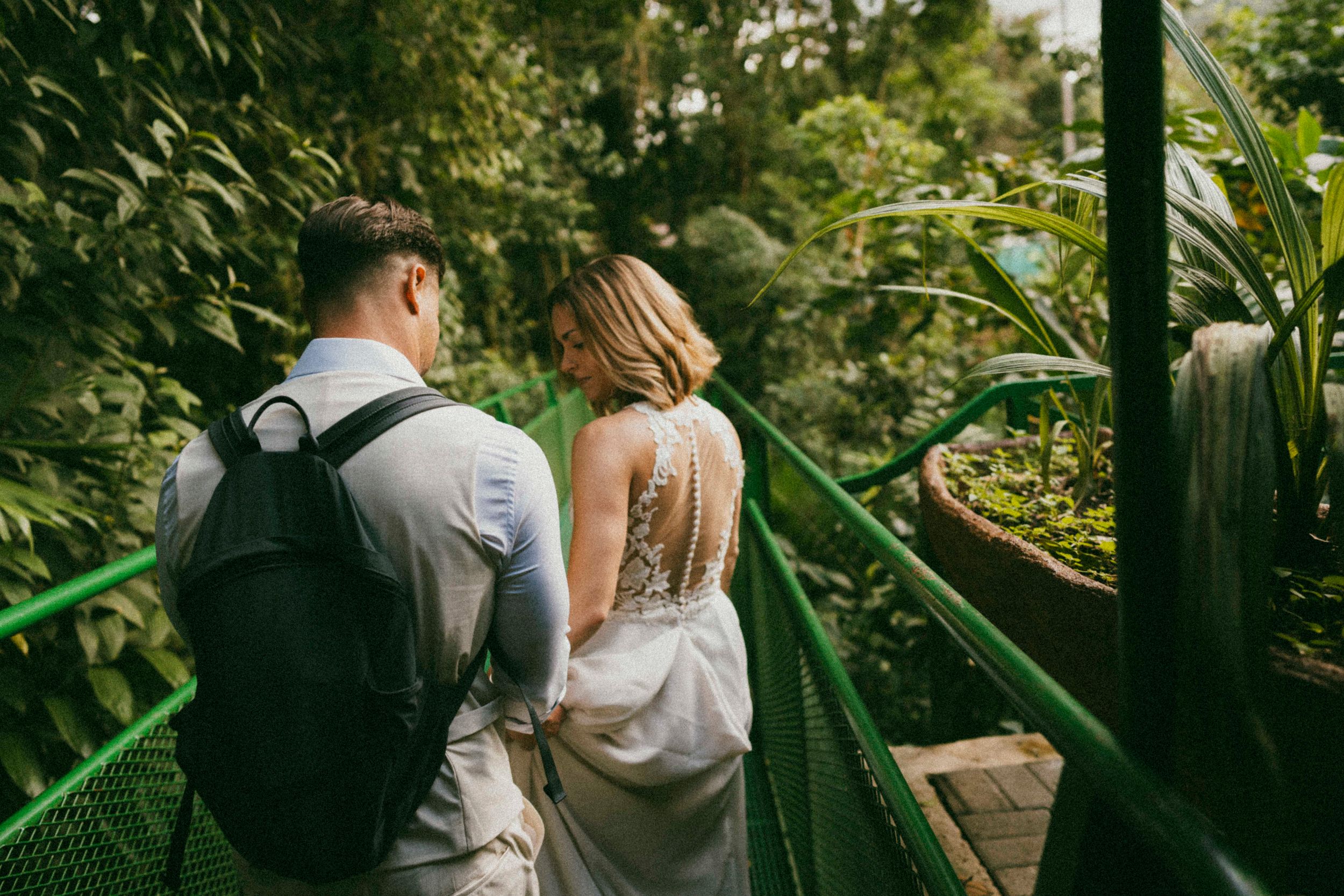 Couple walking through a lush tropical garden path in wedding attire.