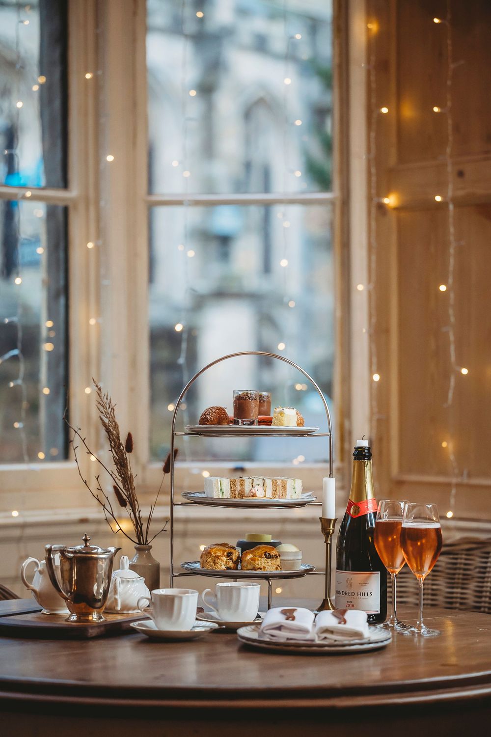 Elegant afternoon tea service with sparkling lights and tiered dessert stands set on a wooden table in a cozy restaurant.