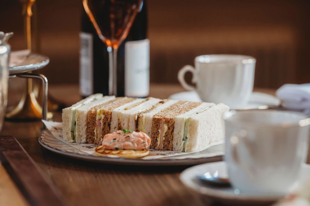 Steaming coffee cup and layered sandwich served on rustic wooden table with natural lighting.