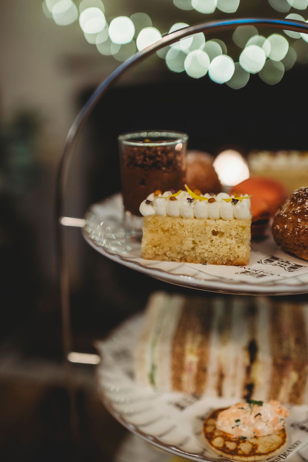 Elegant display of various desserts and cakes on tiered serving platters with lighting effects in the background.