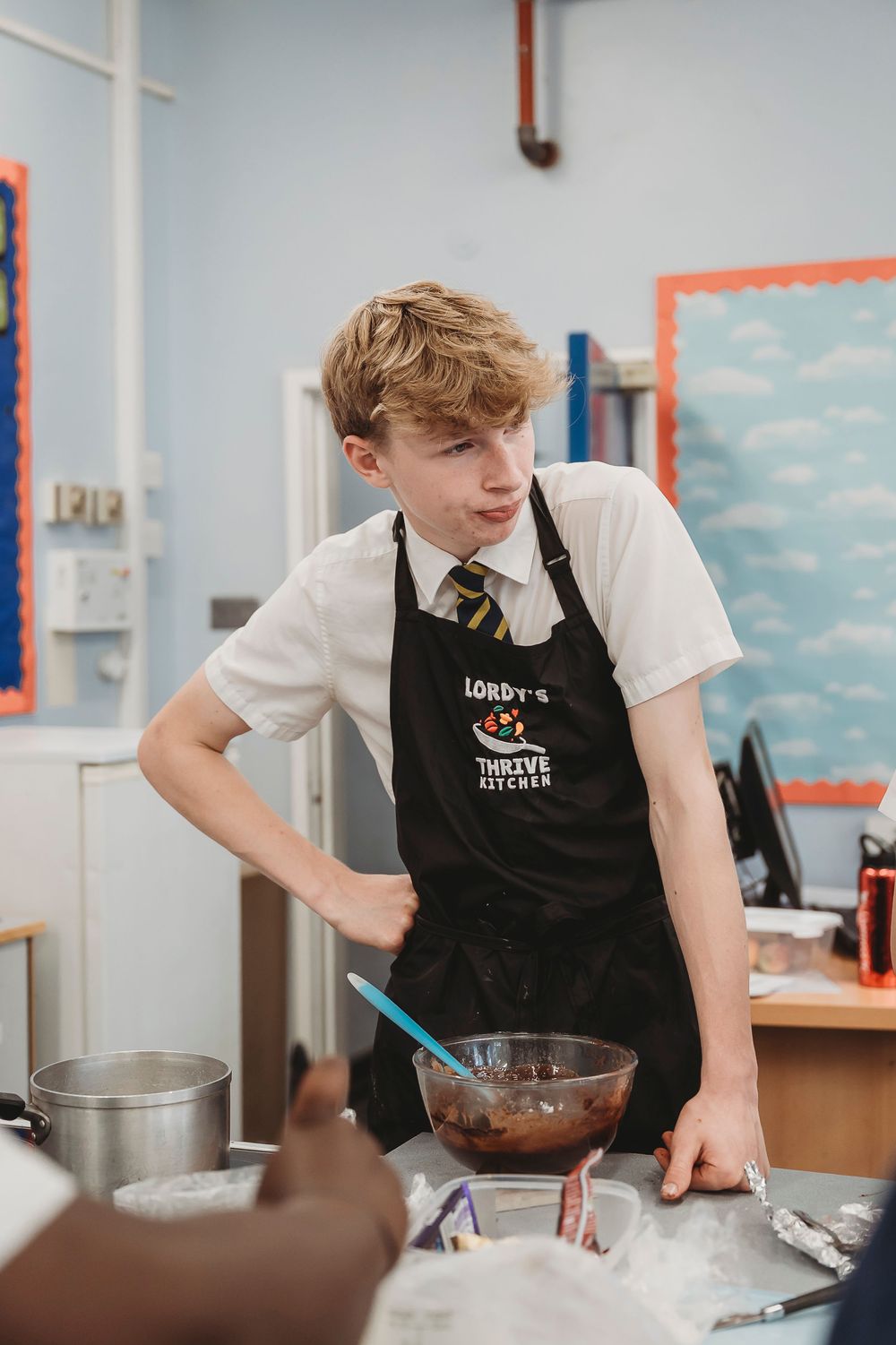 Student wearing a black apron and uniform practices culinary techniques in a teaching kitchen.