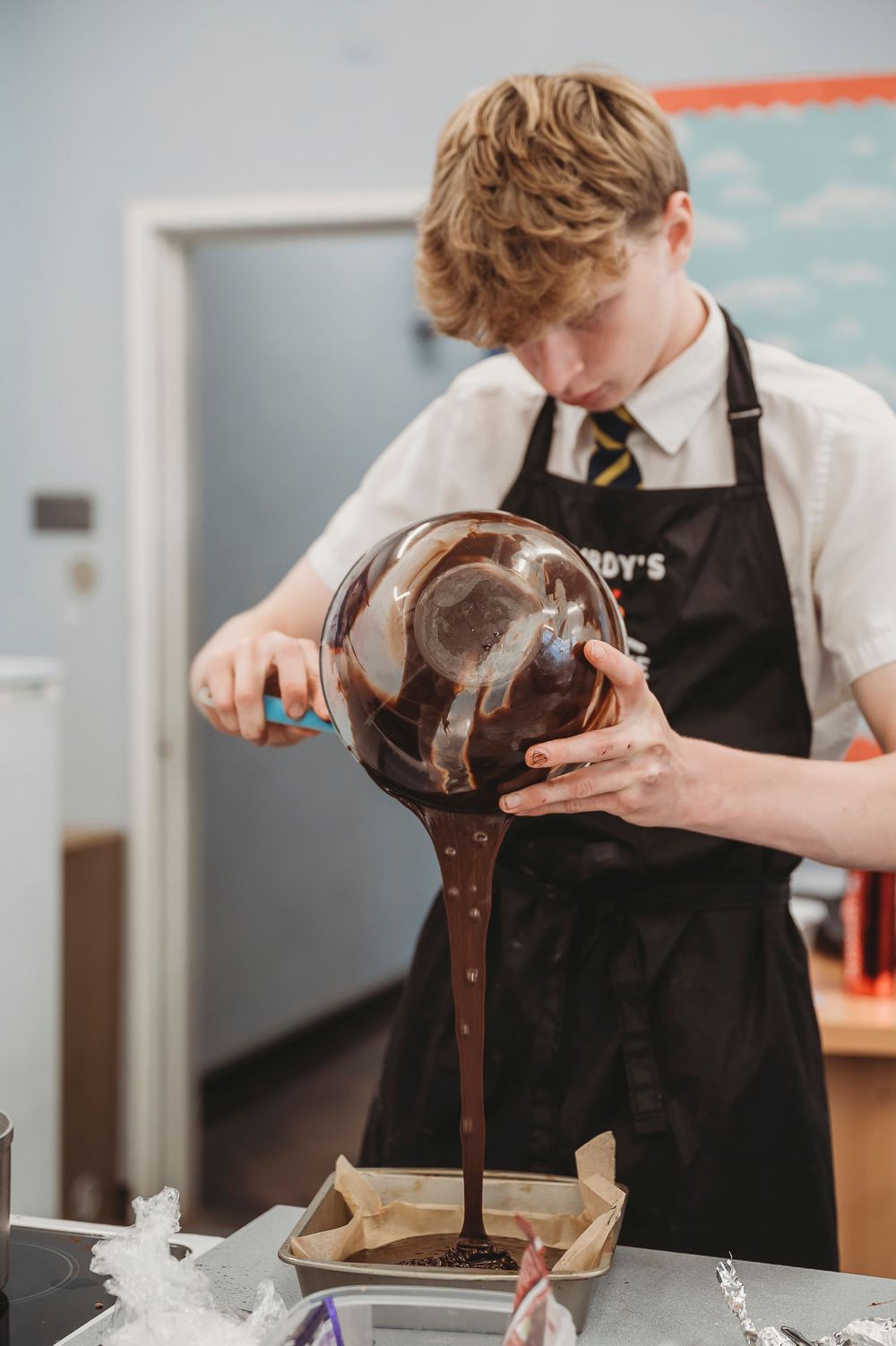 Chocolate sauce being poured from a glass container onto a baking preparation surface.