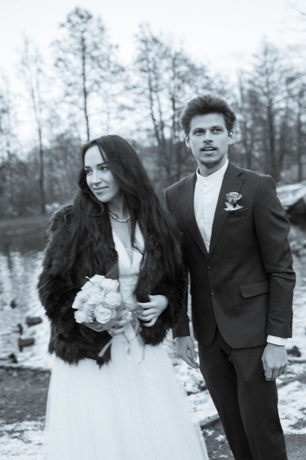 Black and white wedding photo of a couple in winter, bride wearing fur coat with white roses.