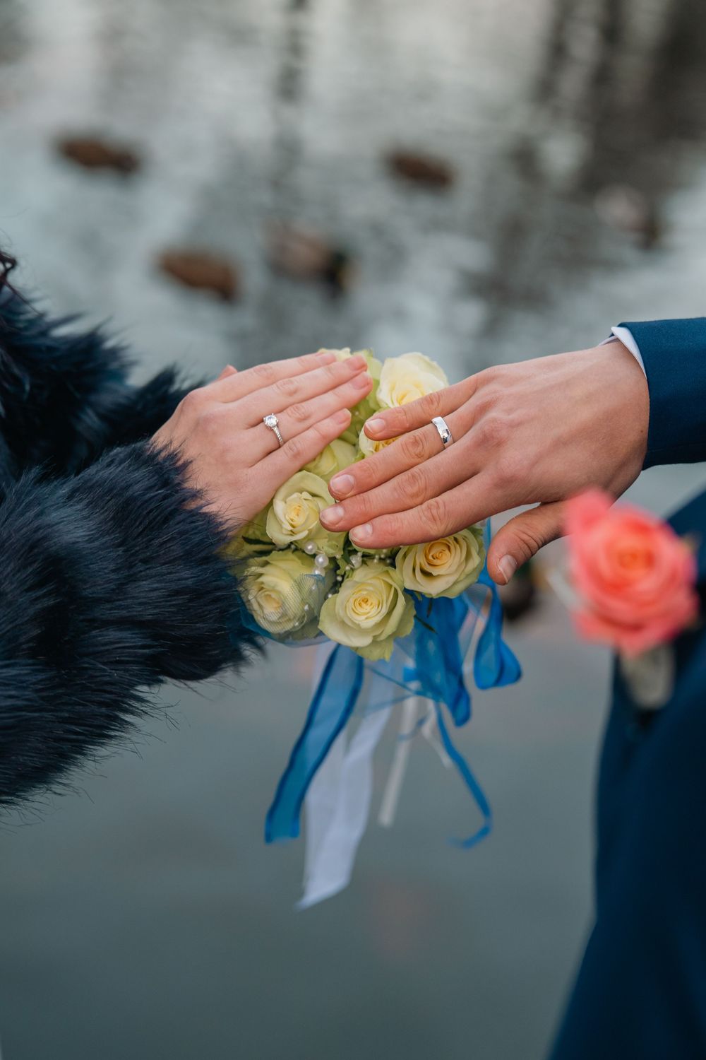 Close-up of hands holding yellow roses with blue ribbon, showing wedding rings.