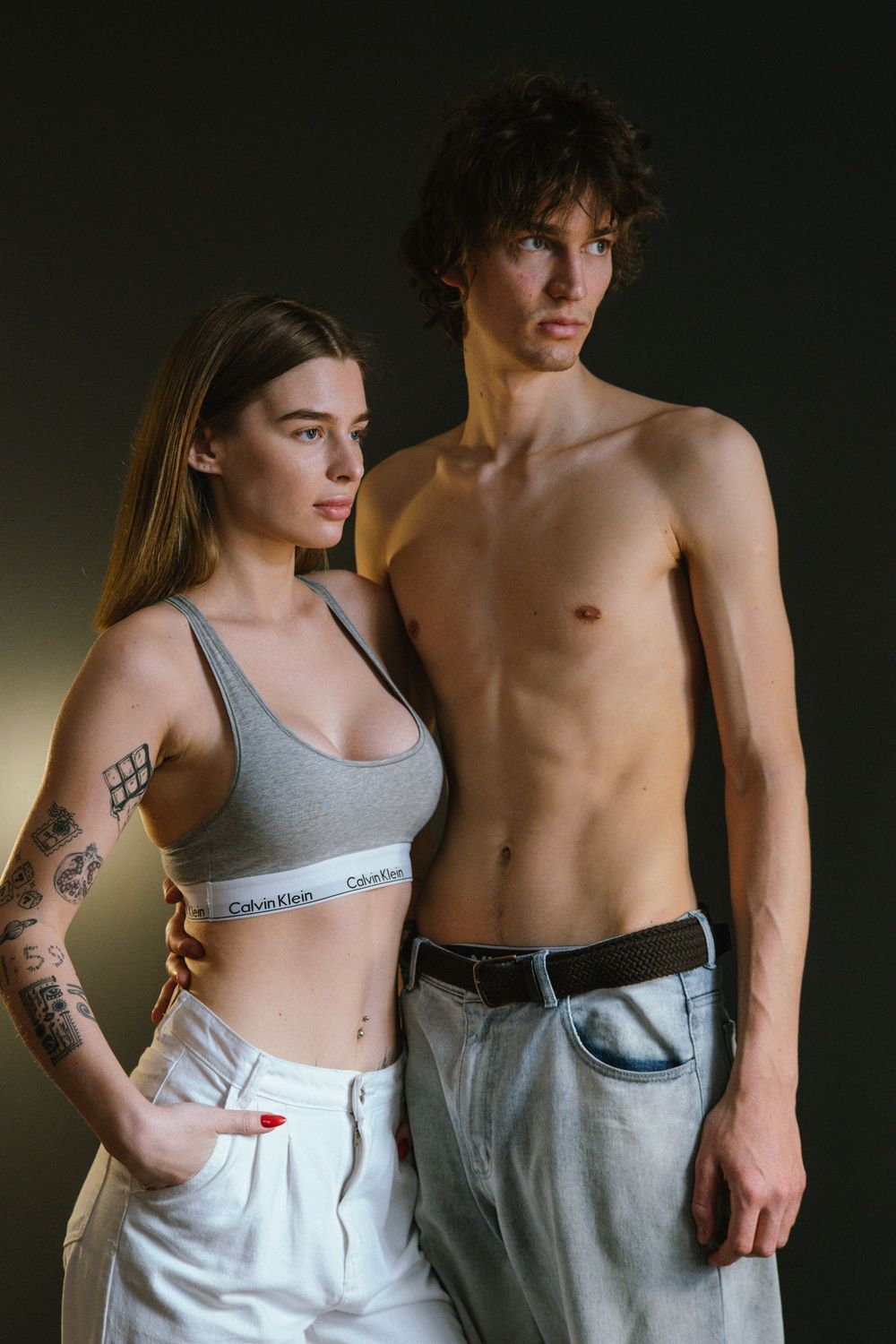 Fashion portrait of a couple in casual attire against dark background showing Calvin Klein sportswear and denim.