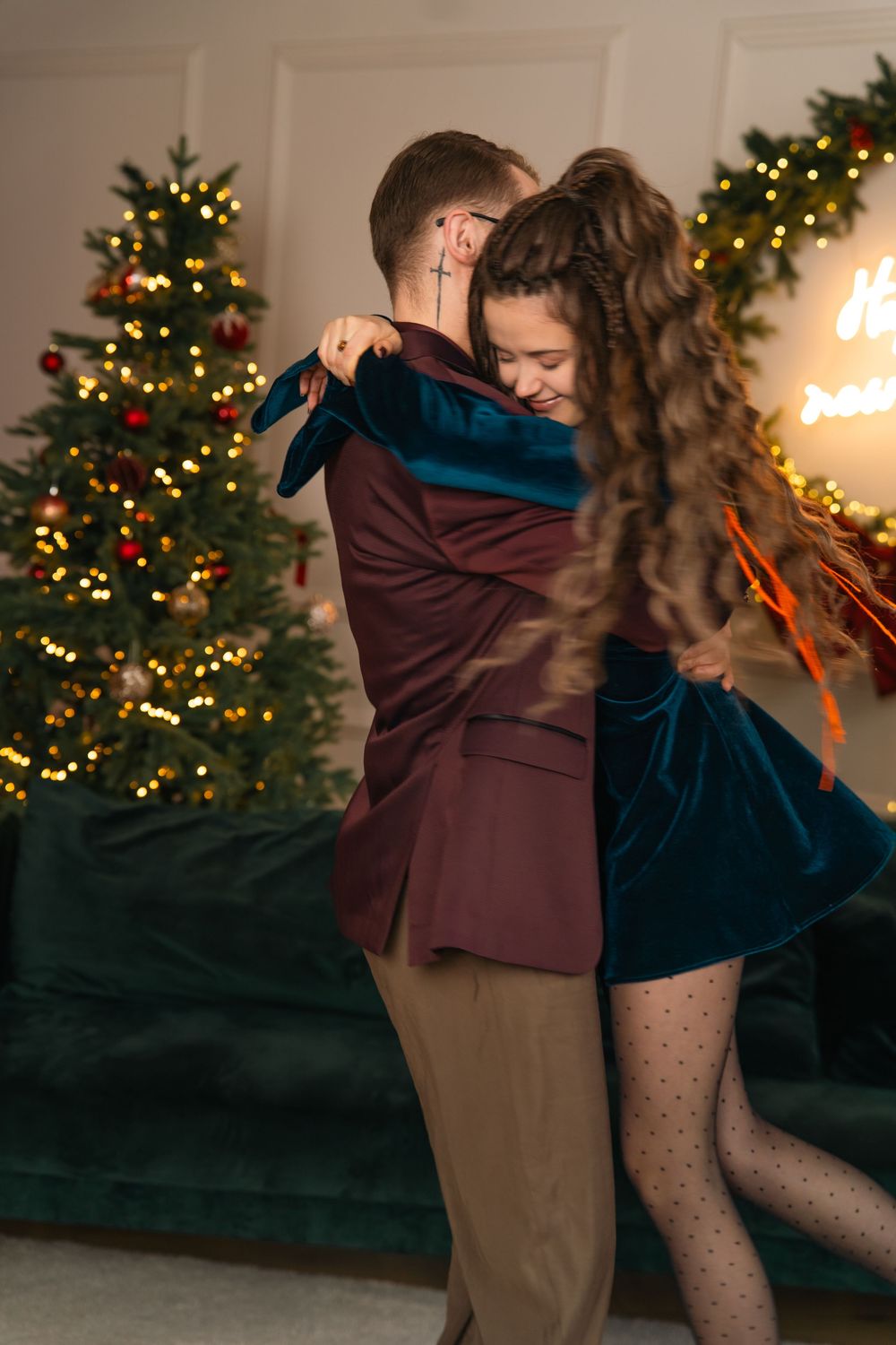 Couple dancing together in front of a decorated Christmas tree with warm lighting and holiday ambiance.