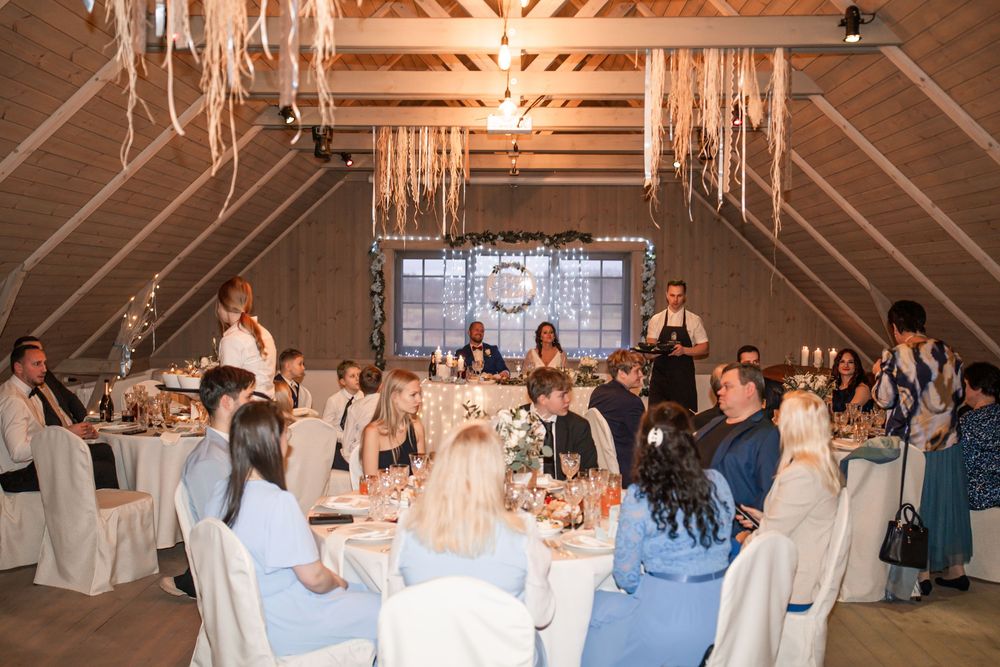 Wedding reception in rustic barn venue with hanging decorations and seated guests.