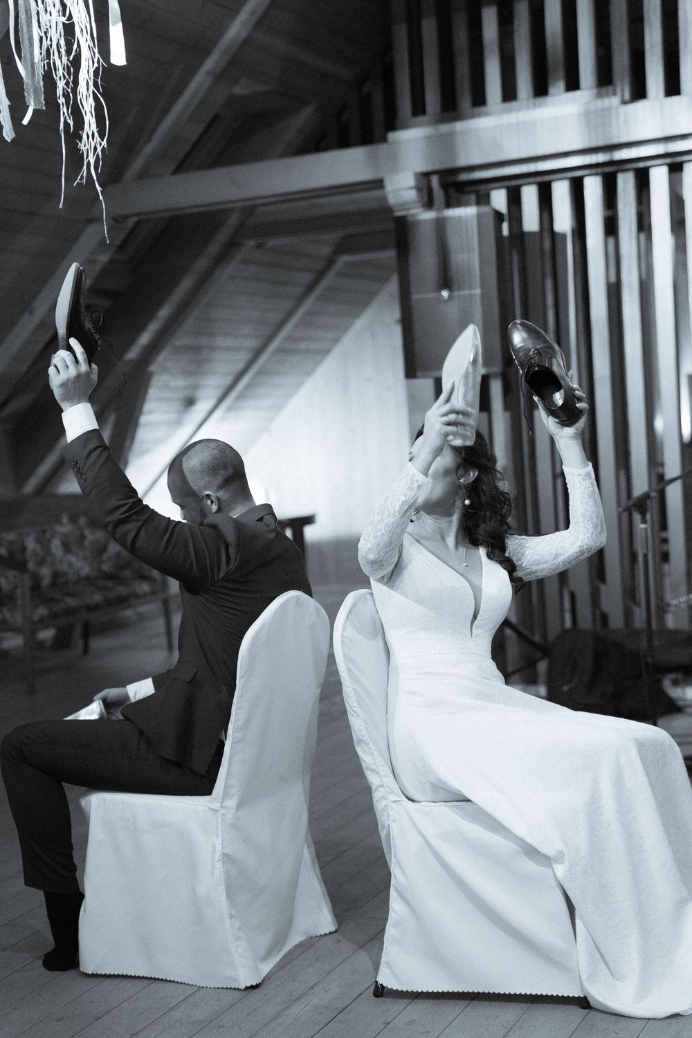 Black and white photo of wedding couple doing synchronized dance moves in chairs.