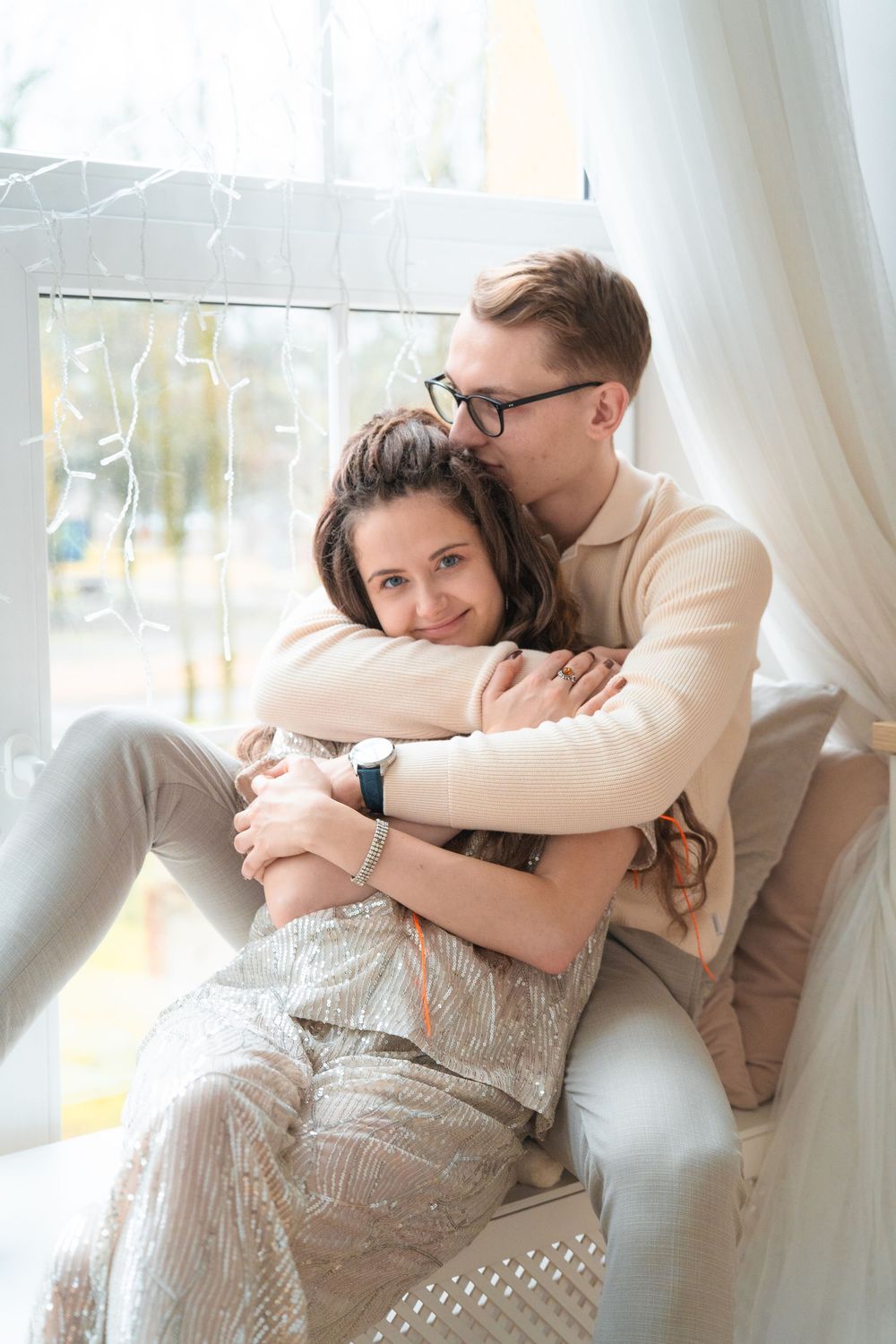 Intimate portrait of couple cuddling by window in casual winter attire.