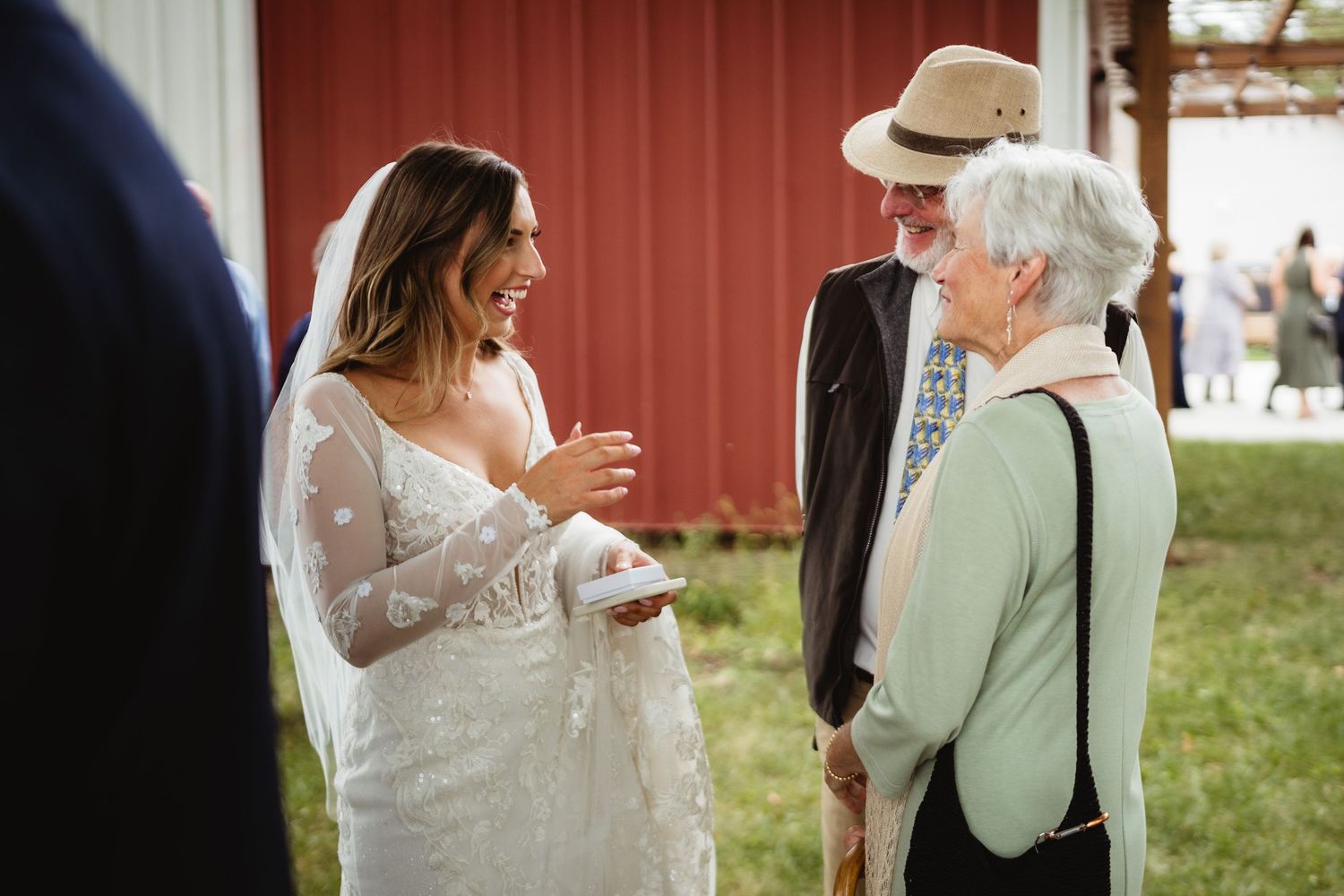 A bride in a flowing white dress dances and twirls on a lawn with a red barn in the background.