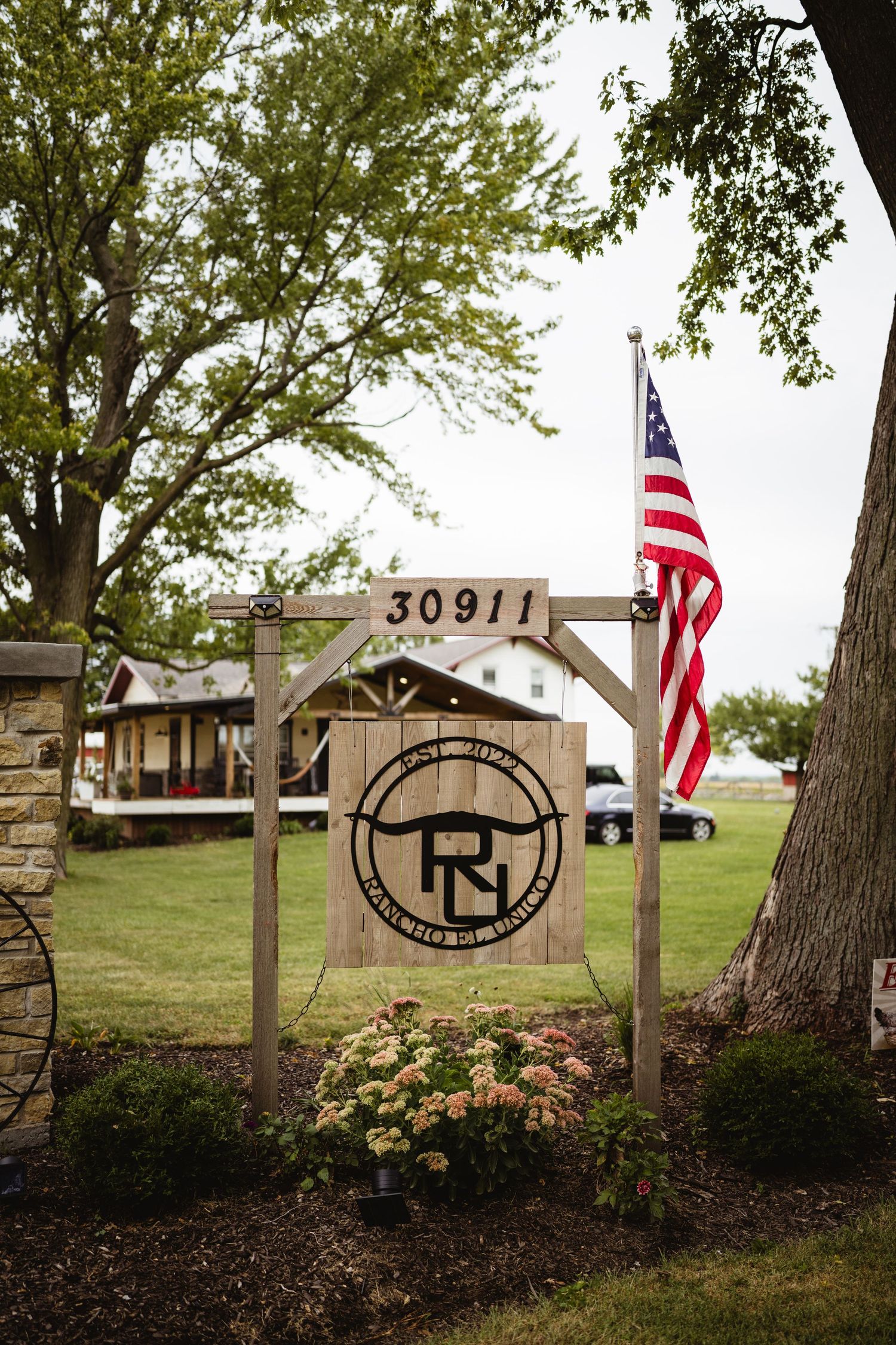 Rustic residential entrance sign with address number 30911 and American flag displays circular logo under wooden arch.