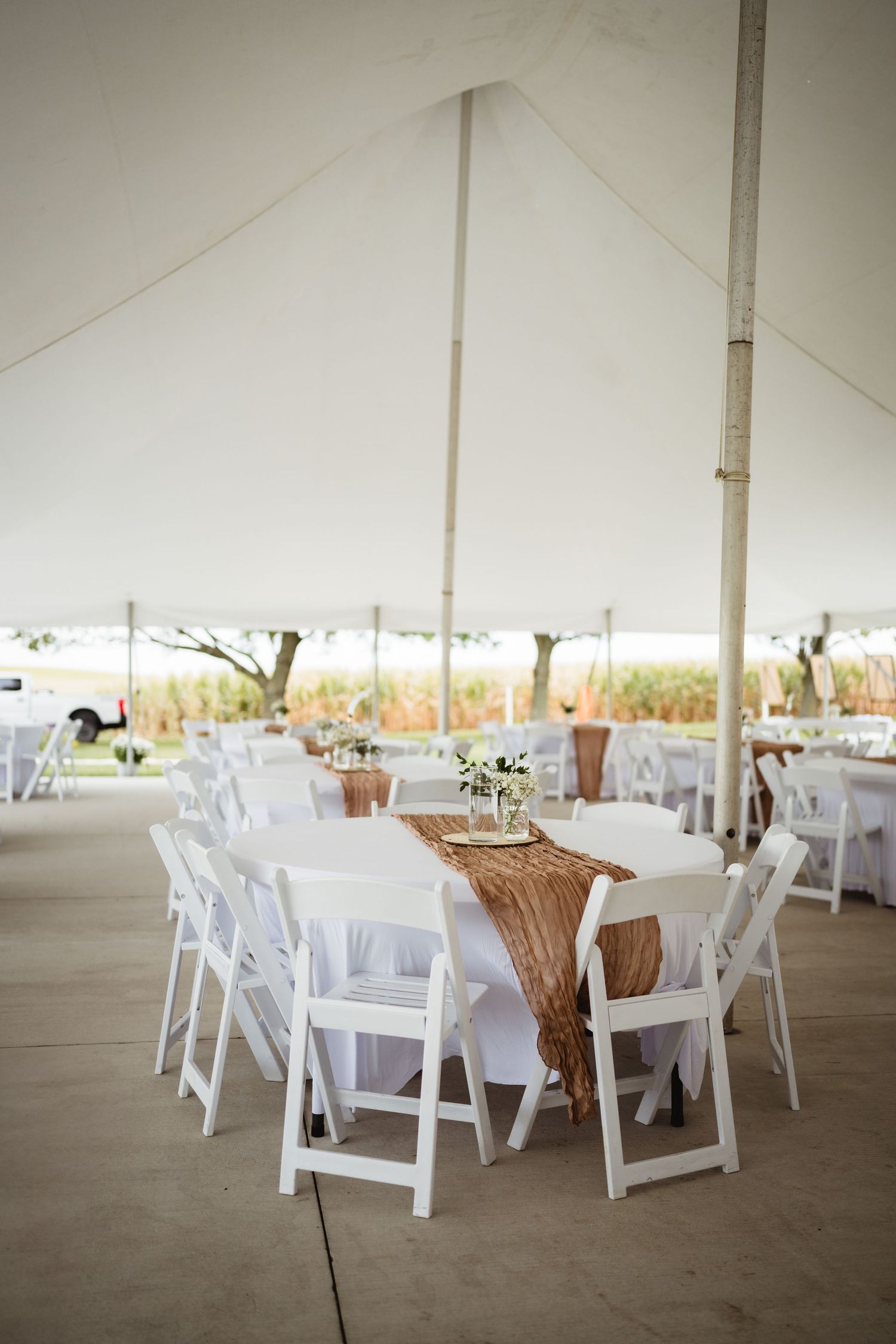 Empty reception tent with round tables and white folding chairs set up under a white canvas canopy for an outdoor event.