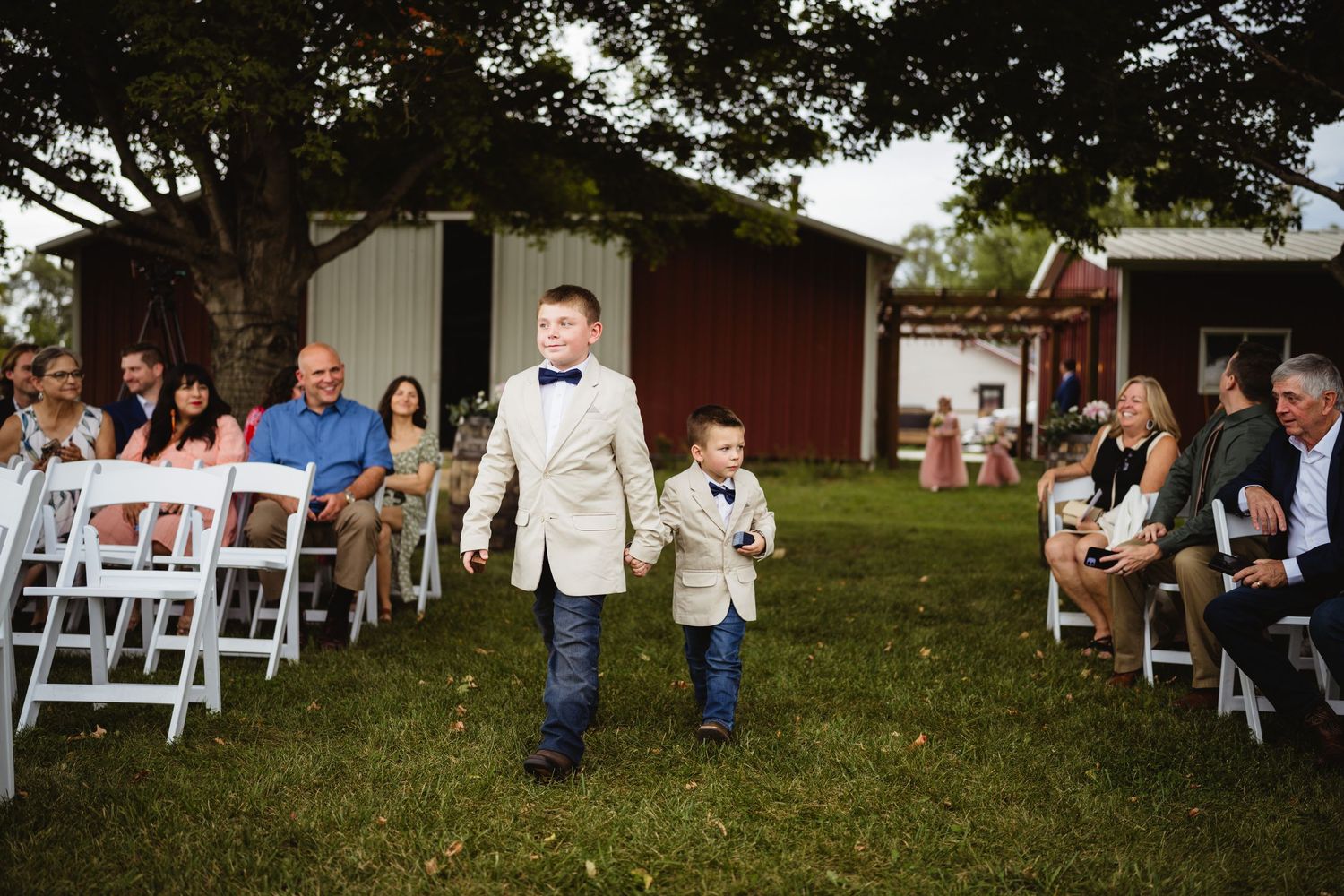 Wedding guests sit on white chairs arranged in rows outdoors on a grassy lawn for a garden ceremony.