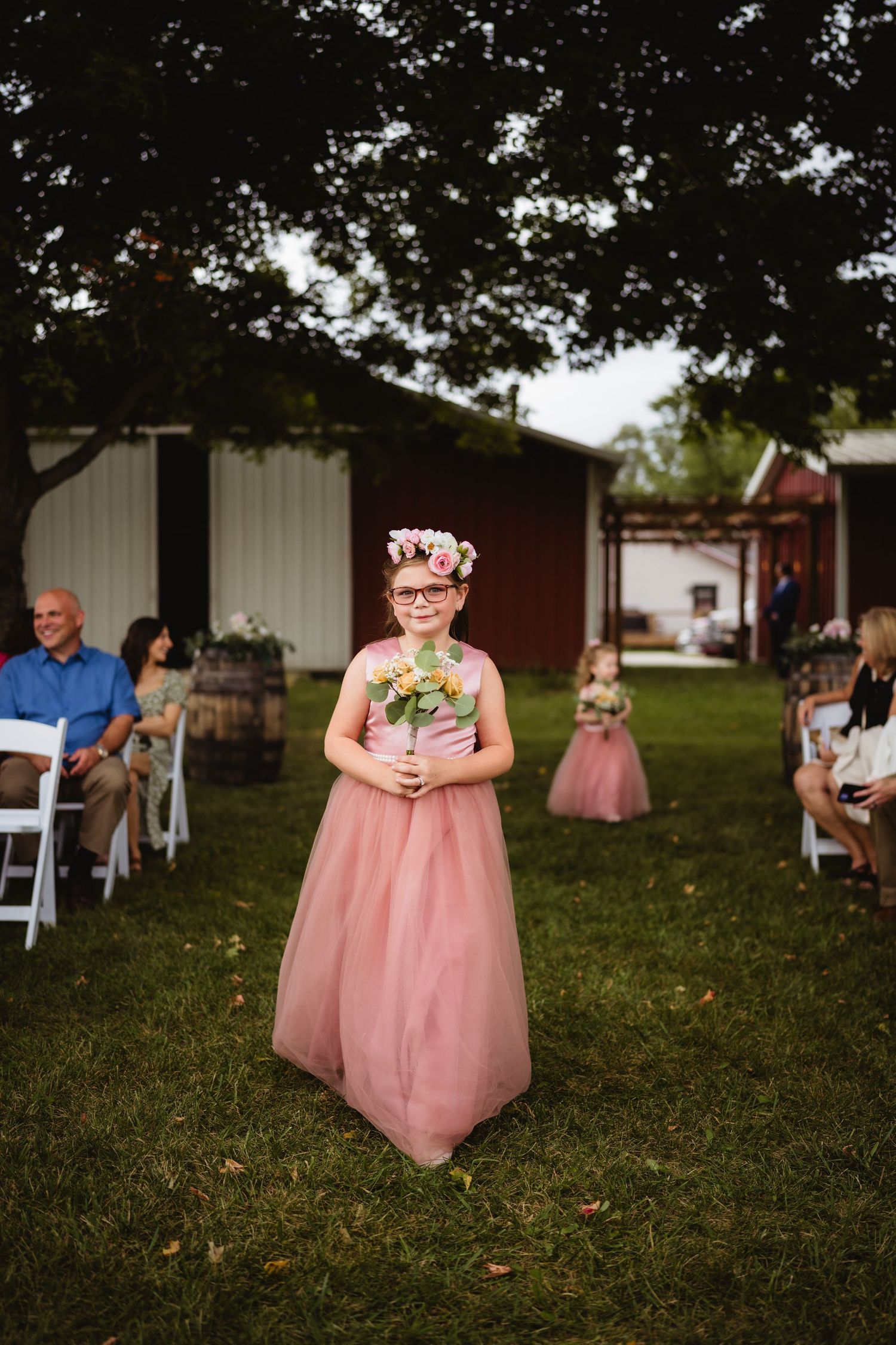 Two pink bridesmaid dresses are visible during an outdoor wedding ceremony on a grassy lawn.