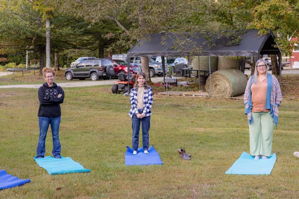 People practicing outdoor yoga or exercise on blue mats in a grassy park area with parked cars in the background.