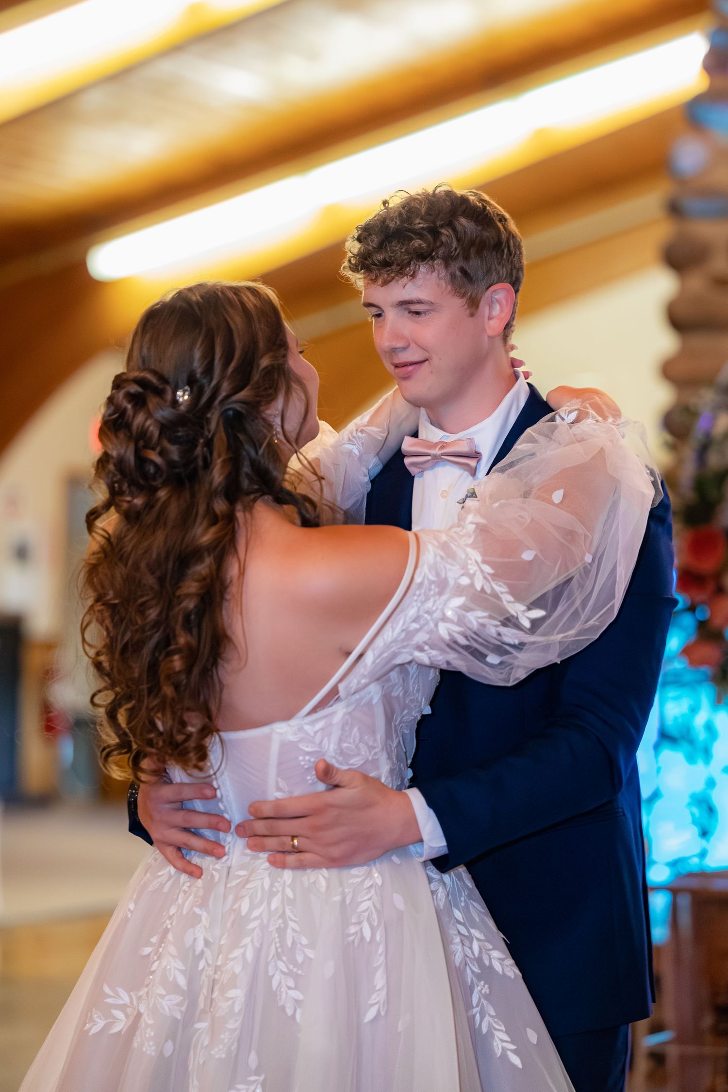 A couple sharing a romantic slow dance at their wedding reception in a warmly lit venue.