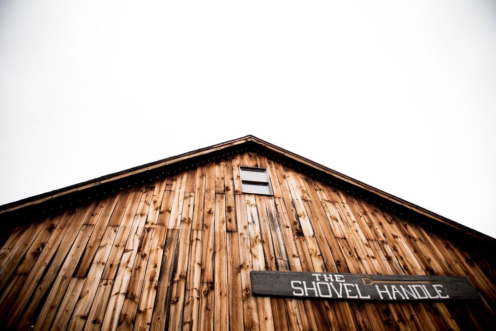Low-angle view of a weathered wooden barn with 'Shovel Handle' text visible on its facade.