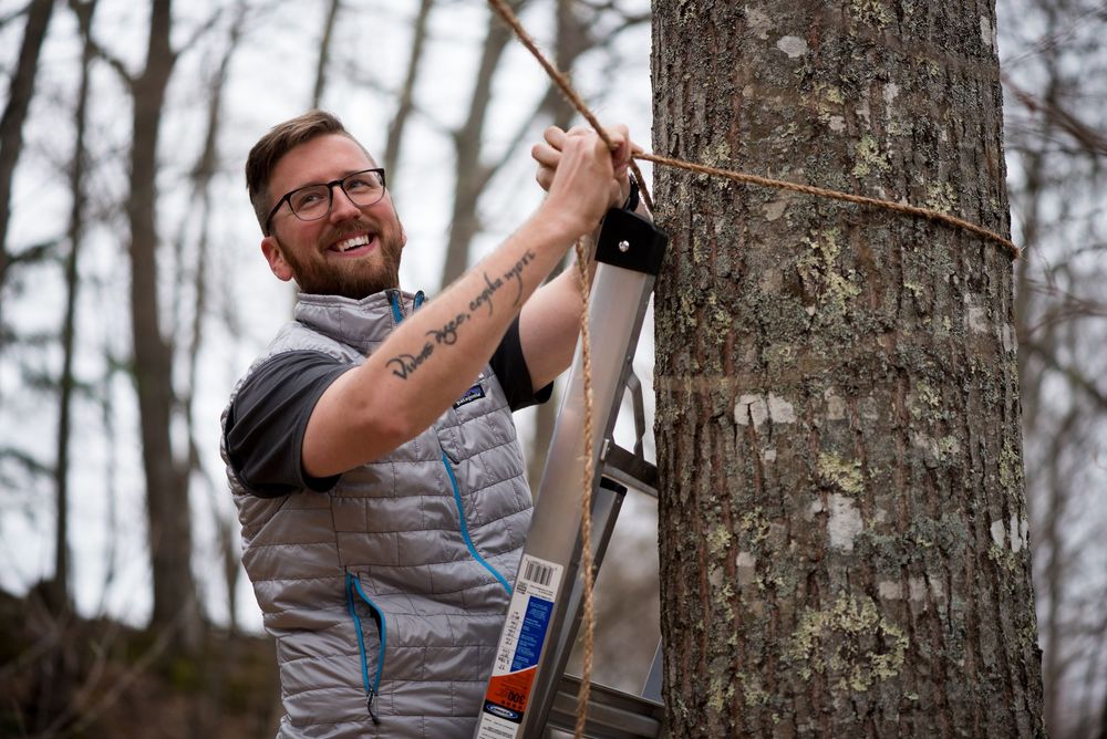 A groom in a gray vest climbs a ladder while preparing their ceremony site.