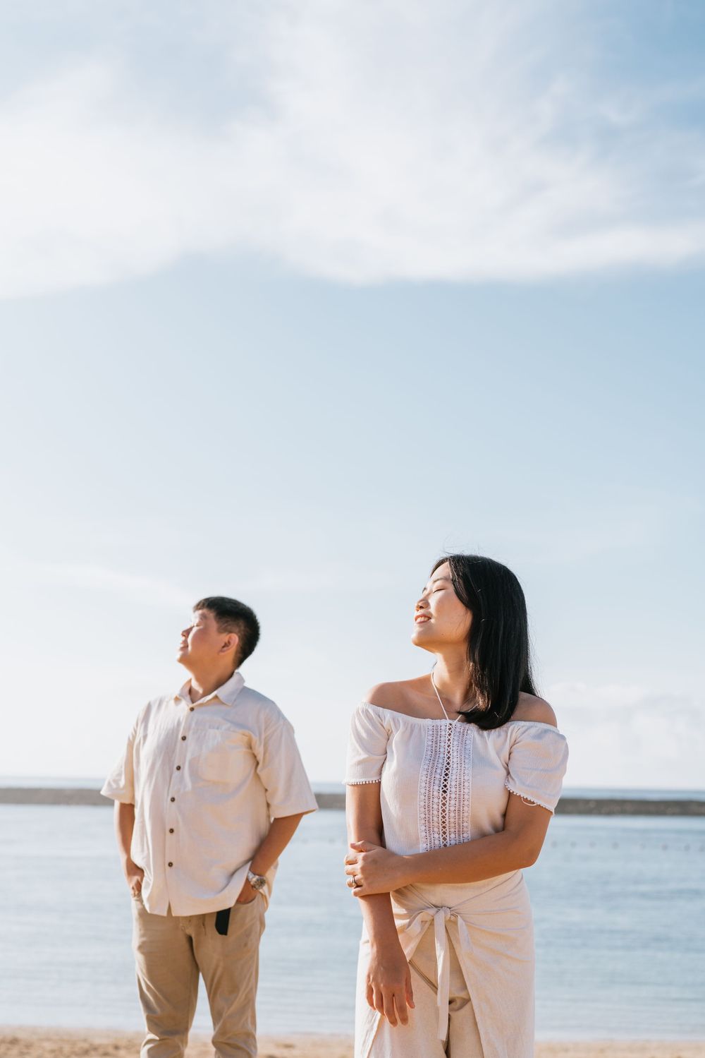 Couple in white attire sharing a playful moment against a bright blue ocean backdrop.