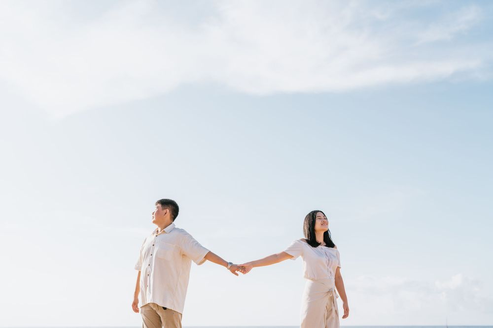 Couple holding hands while walking on a scenic beach path under blue skies.
