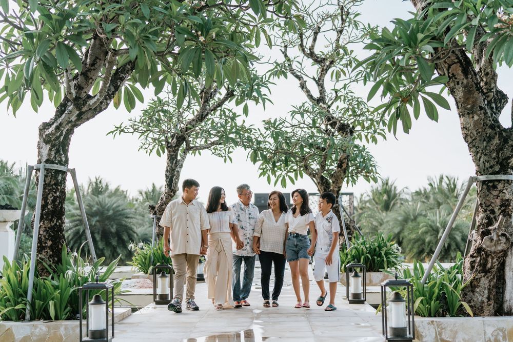 Group photo session under large trees in a lush tropical garden setting.