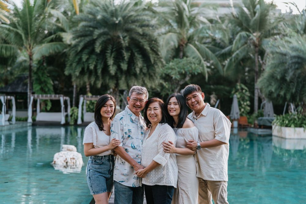 A joyful family gathering by a tropical resort pool surrounded by palm trees and lush greenery.