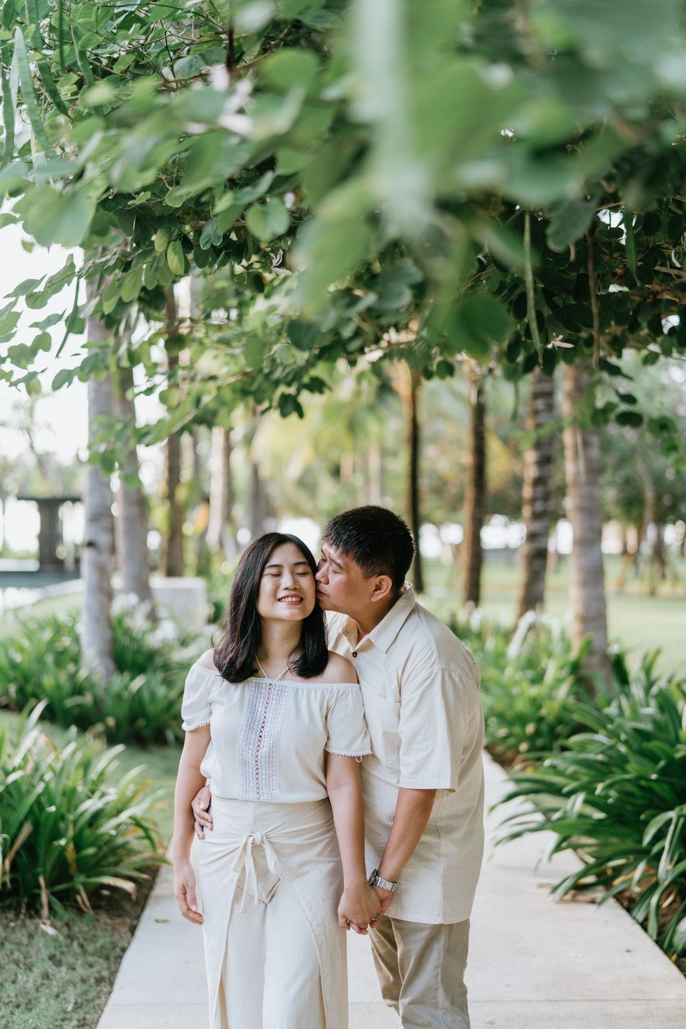 Couple in matching white outfits walking through a lush tropical garden path.