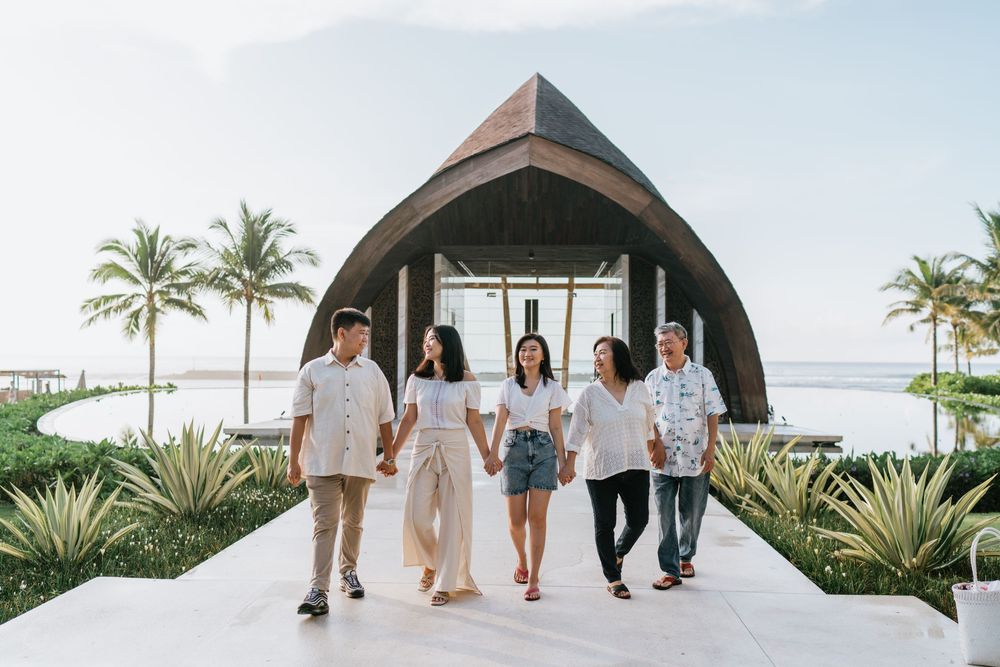 Group walking together along a scenic beachfront path with palm trees and resort architecture.