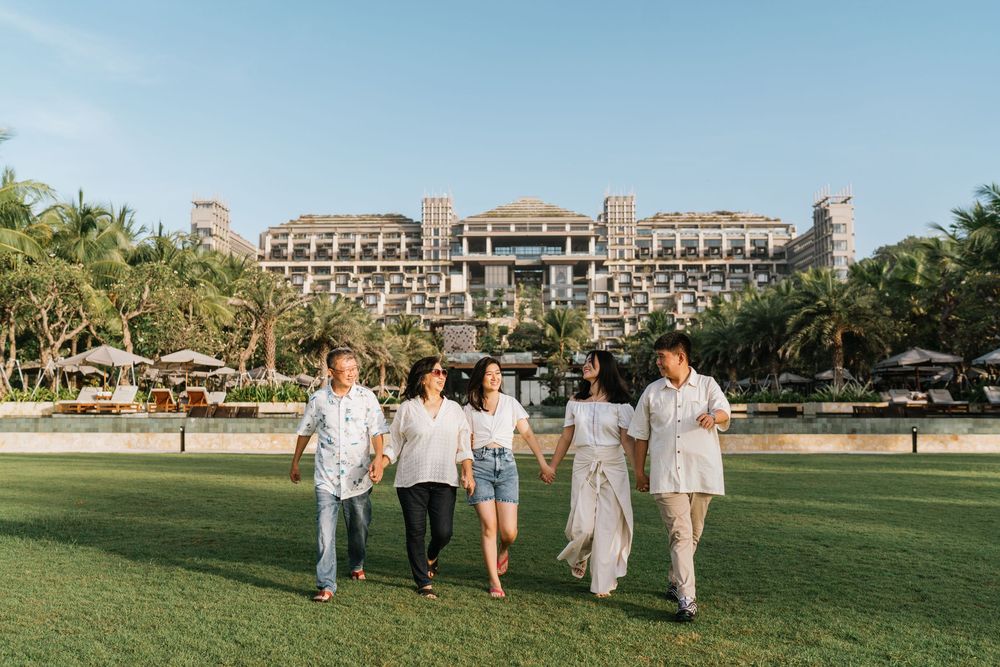 Family group walking together on manicured resort grounds with palm trees and buildings.