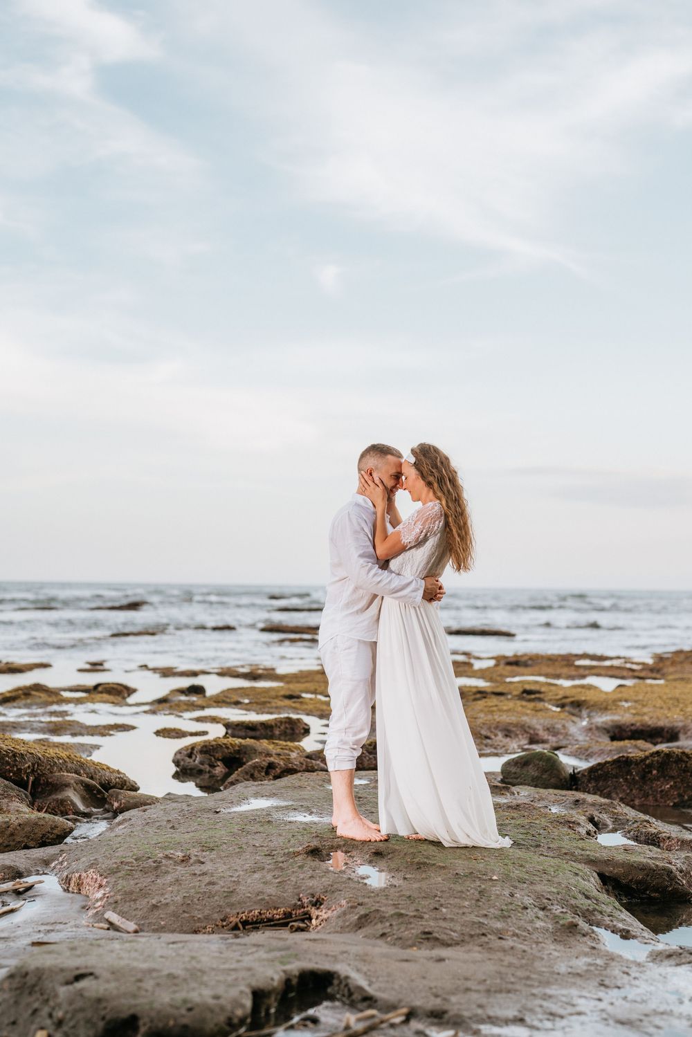 A romantic moment captured on rocky shores with ocean waves in the background.