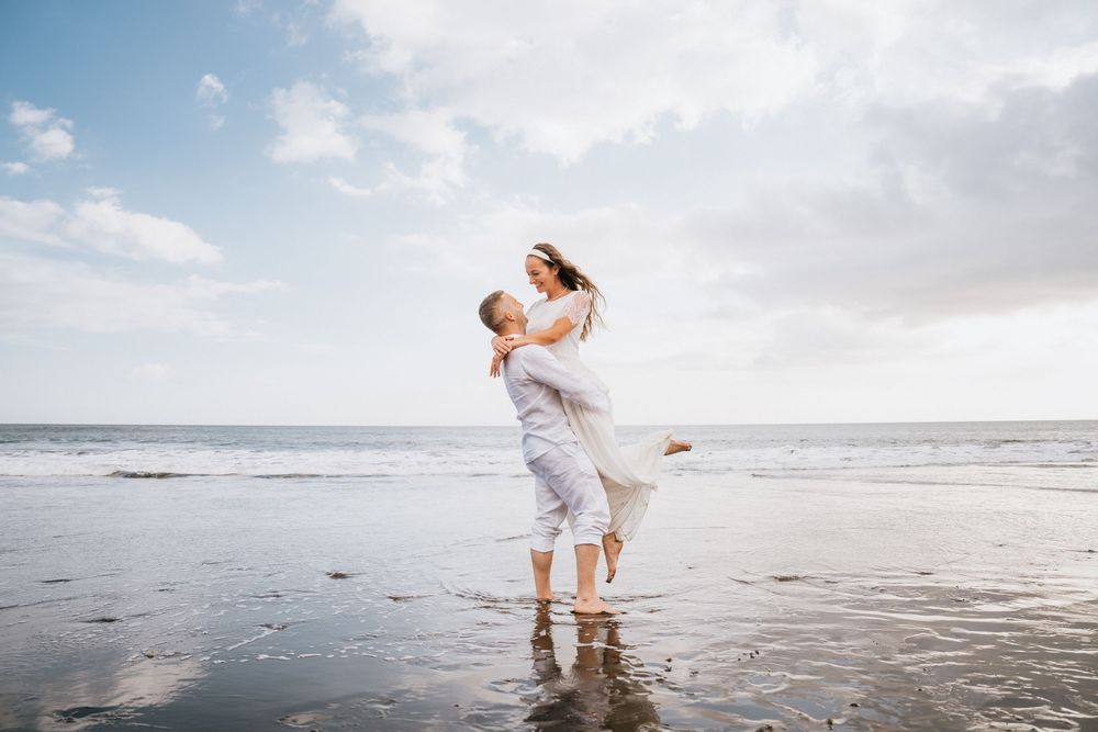 Two people in white clothing dance and play on a misty beach at sunset.