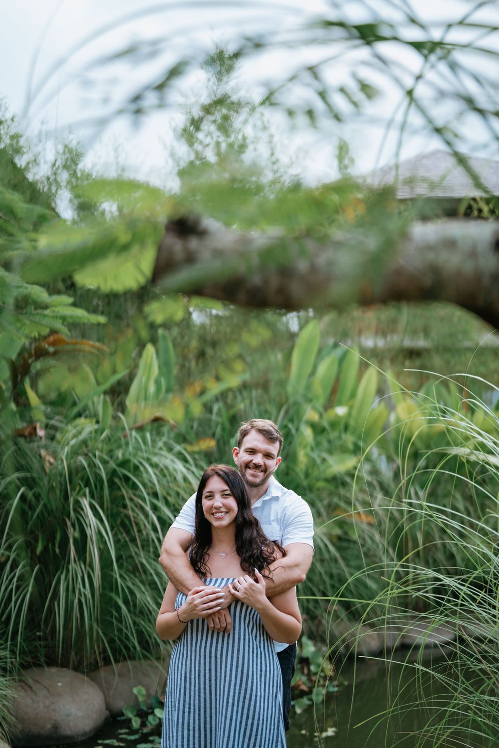 A romantic moment captured in a lush garden setting with tall grass and tropical plants.