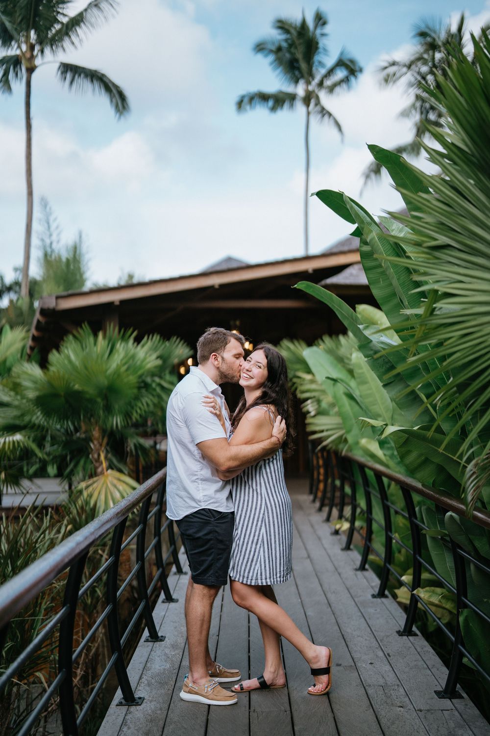 A romantic scene on a wooden boardwalk with palm trees and tropical foliage in the background.