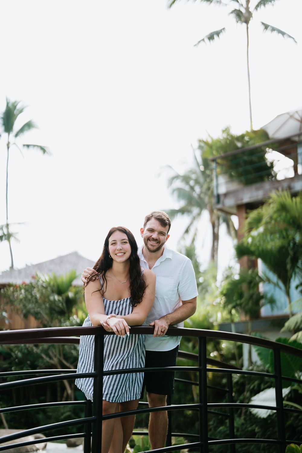 A couple shares a joyful moment on a bridge surrounded by palm trees and tropical landscaping.