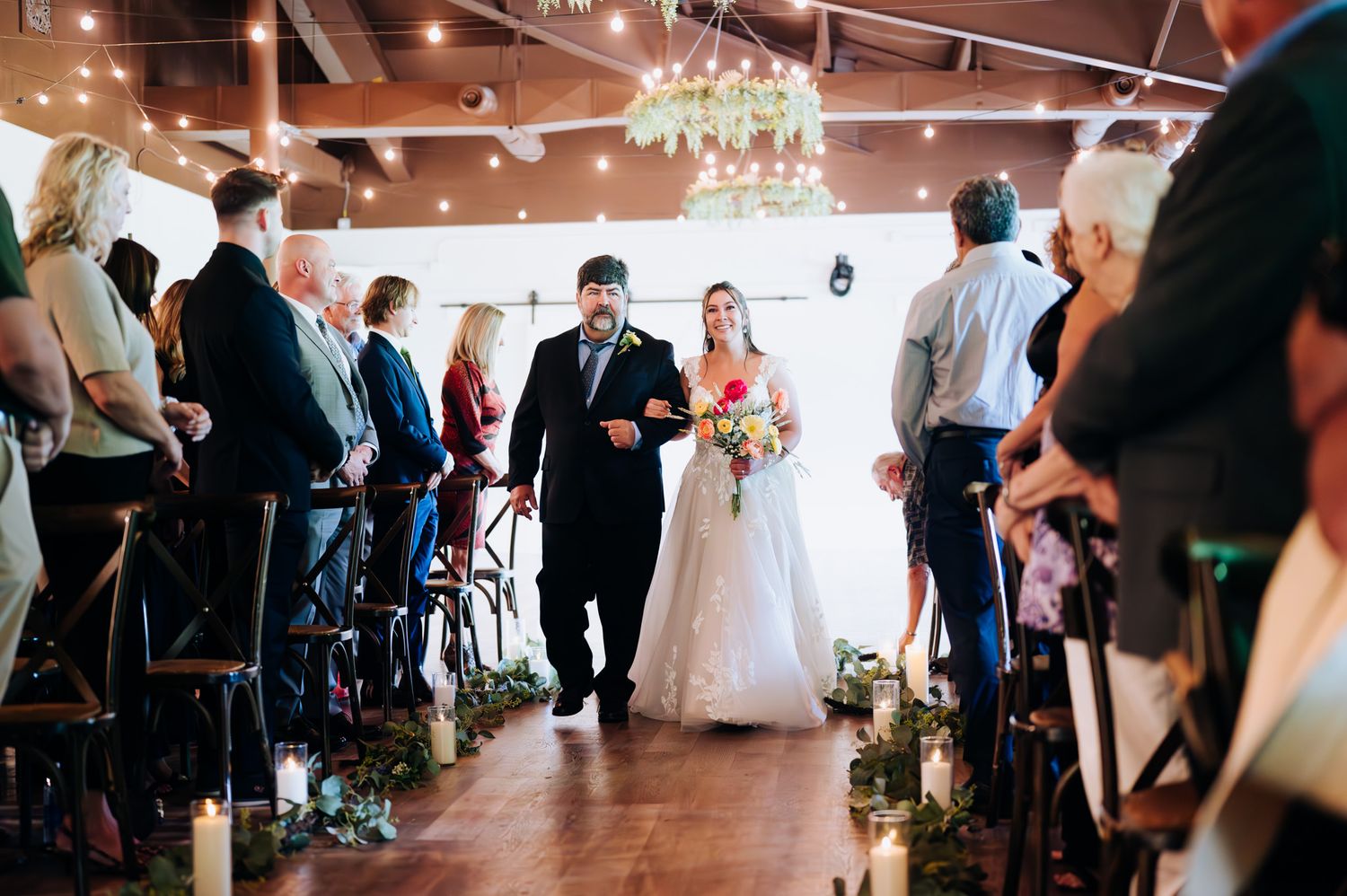 A group of people gathered in a gallery space with white walls and wooden floors during a social event.