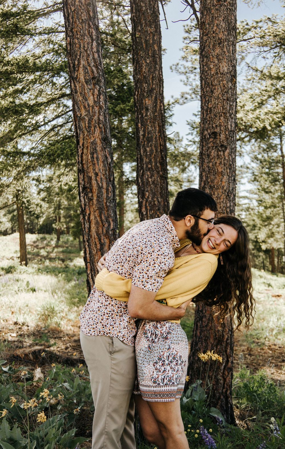A couple dances playfully among pine trees and purple wildflowers.