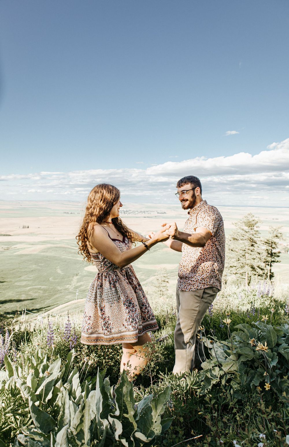 A couple dances together on a hilltop overlooking a vast valley landscape.