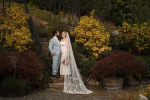 Elegant wedding couple embraces in an autumn garden with vibrant yellow and red foliage creating a romantic backdrop.