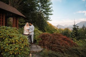 A serene Japanese garden with red maple trees and traditional wooden structures overlooks a tranquil mountain landscape.