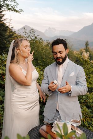 A couple in wedding attire at an outdoor mountain venue share an emotional moment during the ceremony.