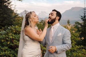 Two newlyweds share a joyful candid moment together outdoors with mountain peaks and evergreen trees in the background.